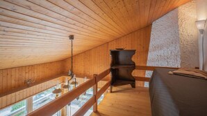Een houten interieur met schuine wanden, een bed, een kleine tafel en uitzicht door een raam.