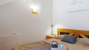 A bedroom with a wooden headboard, a bedside table with a lamp, a tray with a kettle and cups, and a wall-mounted light fixture. - Pierres Blanches F et H by Interhome (Les Contamines)