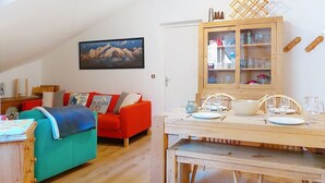 A cozy living room with a red sofa, a wooden dining table set for two, and a wooden cabinet above the table. - Pierres Blanches F et H by Interhome (Les Contamines)