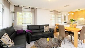 Ein modernes Wohnzimmer mit einer schwarzen Couch, einem Glastisch und einem Essbereich mit Holztisch und Stühlen.