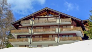 Ein mehrstöckiges Gebäude mit hölzernen Balkonen, wahrscheinlich ein Hotel oder Resort, gelegen an einem verschneiten Hang.