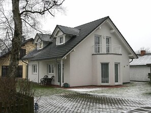 A two-story house with a gabled roof, a balcony on the second floor, and a paved driveway.