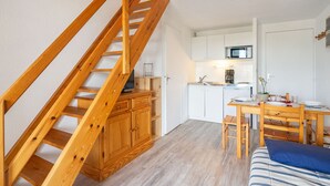Un espacio habitable compacto con una escalera de madera, kitchenette, zona de comedor y cama.