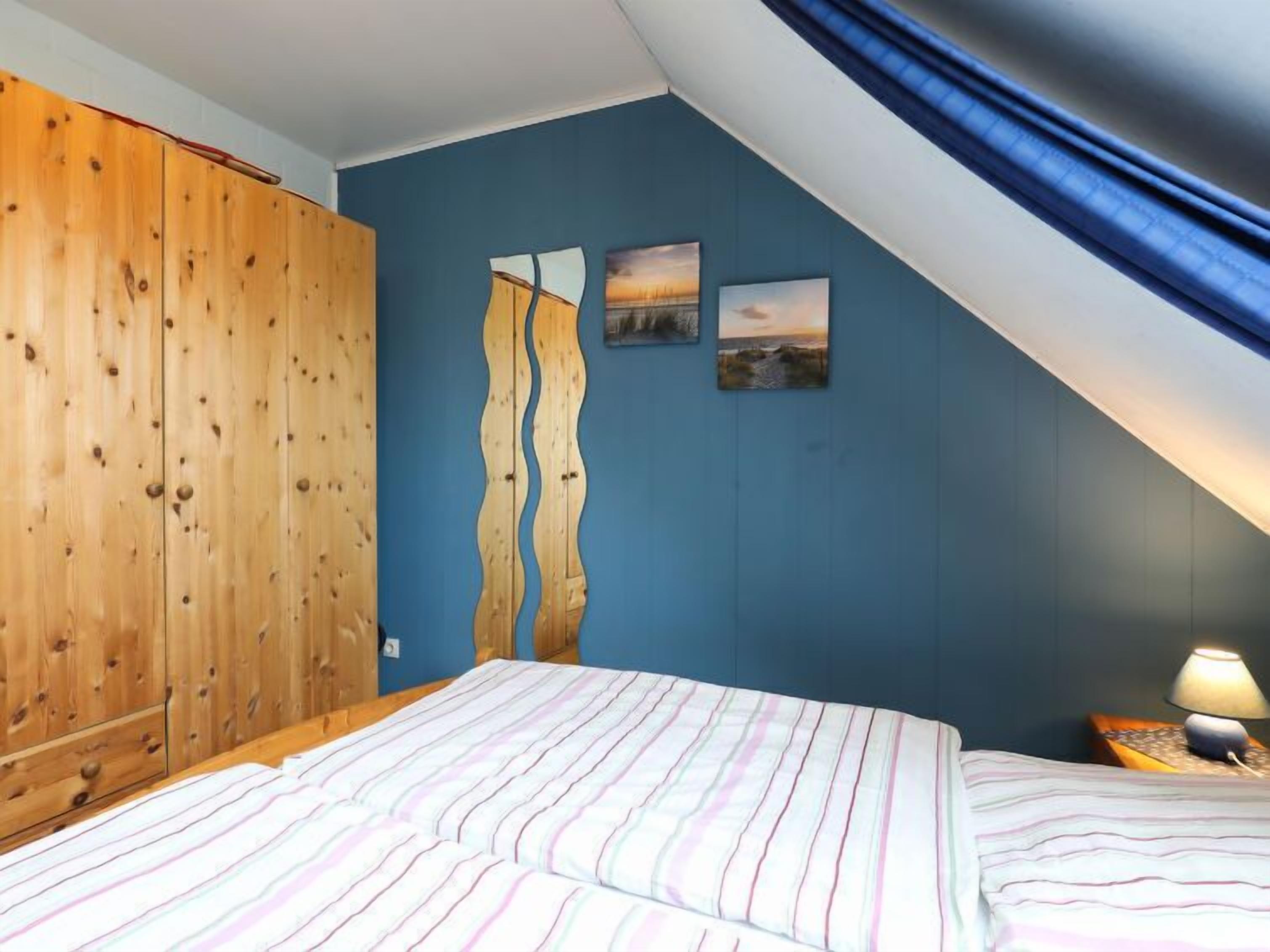 Une chambre avec une armoire en bois, un lit avec une literie à rayures et deux tableaux accrochés au mur.