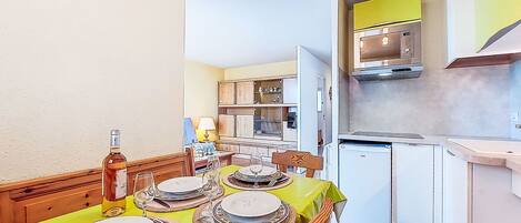 A dining area with a table set for four, a kitchen with white cabinets and a yellow backsplash, and a living area with a sofa and a lamp.