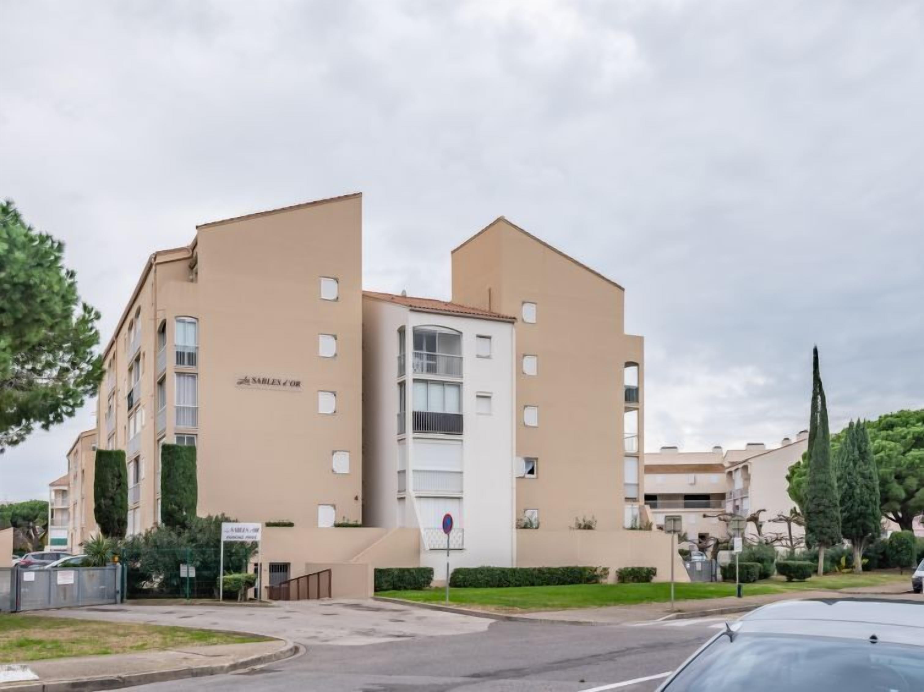 En fleretagers boligbygning med en beige facade, flere balkoner og en lukket indgang.