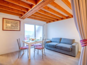 Una habitación acogedora con techo de madera, una mesa de comedor con sillas, un sofá gris y un ventanal con vistas.