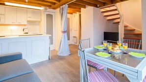 A modern kitchen with white cabinets, a dining area with a glass table, and a staircase leading to an upper level. - Les Reflets de Carnac by Interhome (Carnac)
