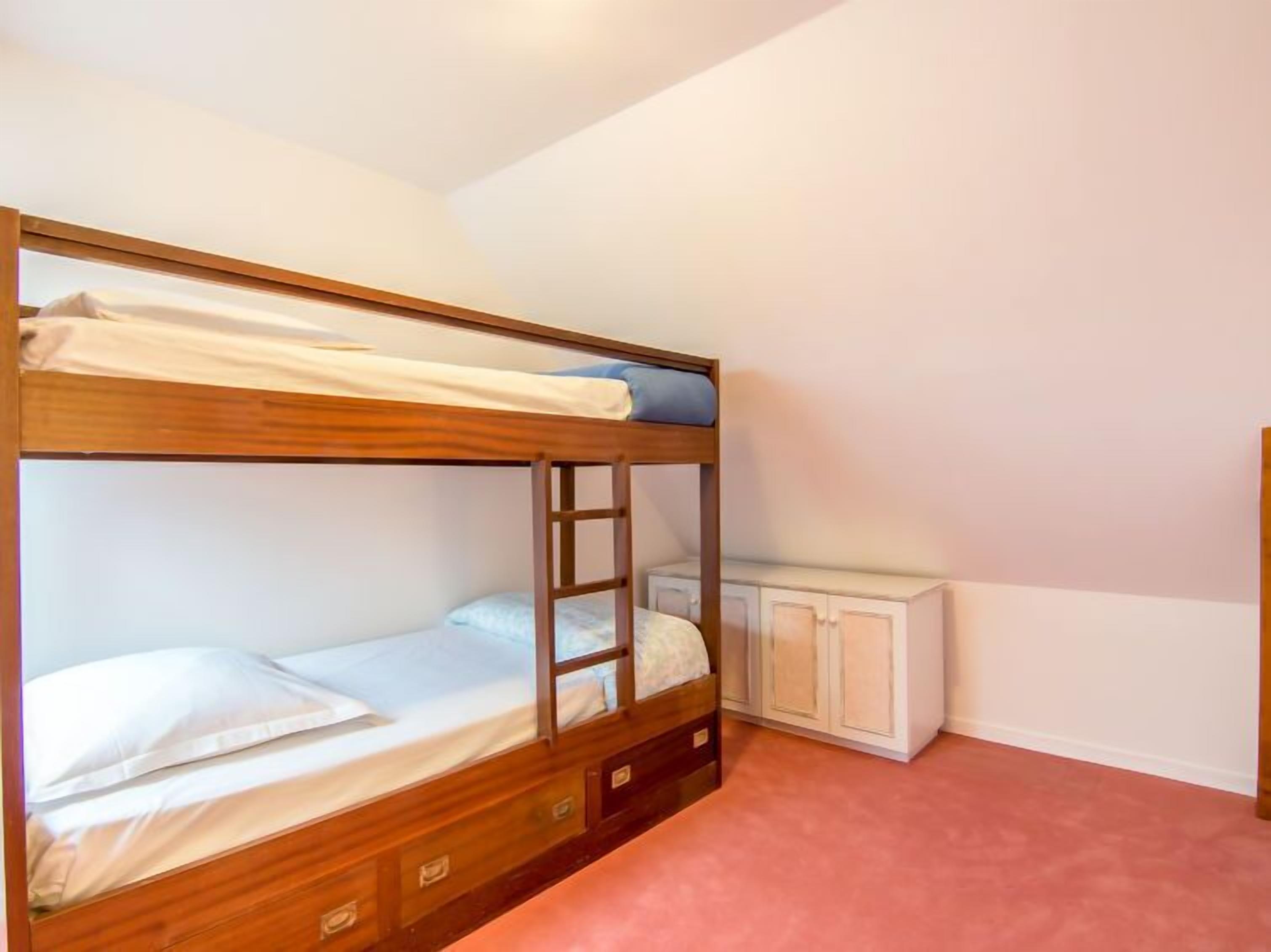 A bunk bed room with a ladder, a small cabinet, and a pink carpet.
