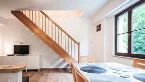 A modern kitchen with wooden flooring, a dining table with placemats, a TV on a cabinet, and a staircase. - Lanovka by Interhome (Jachymov)