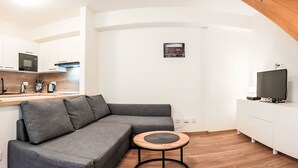 A modern living room with a grey sectional sofa, a small round table, a television, and a kitchen area with white cabinets and a wooden countertop. - Lanovka by Interhome (Jachymov)