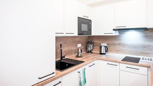 A modern kitchen with white cabinets, a black sink, a stainless steel kettle, and a microwave. - Lanovka by Interhome (Jachymov)