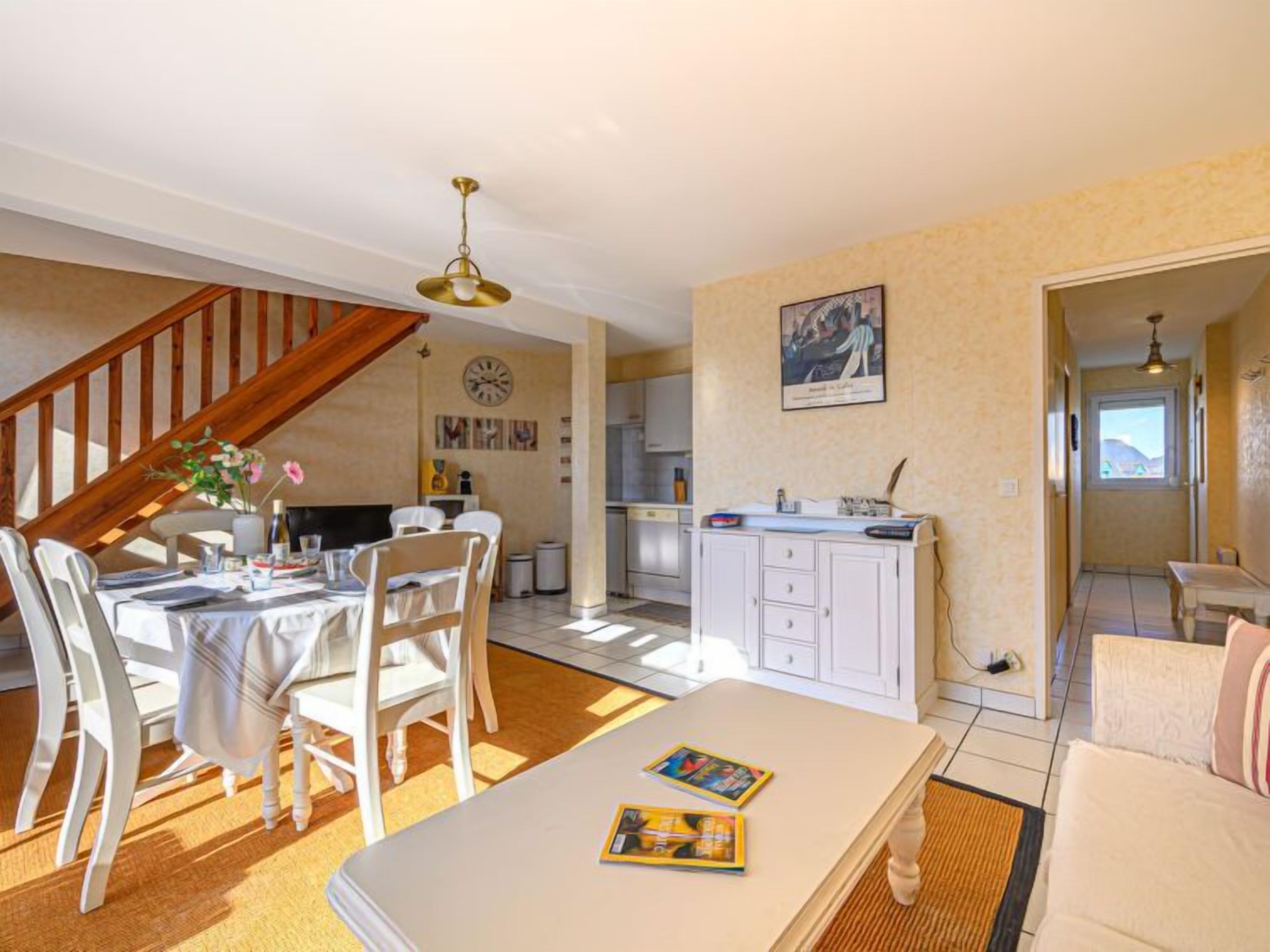 A spacious living area with a dining table, chairs, a sofa, and a kitchen in the background.