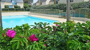 A swimming pool surrounded by lush greenery and a fence, with houses in the background. - Les Villas de Kermaria by Interhome (Quiberon)