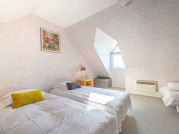 A bedroom with two beds, a window, a painting, and a lamp.