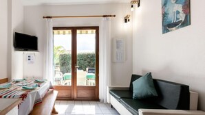 A room with a dining table set for four, a sofa, a television, and a sliding glass door leading to an outdoor area with a table and chairs. - Plage sud by Interhome (Capbreton)
