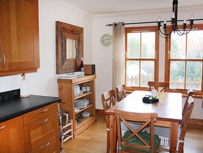 A kitchen with wooden cabinets, a dining table with chairs, a window with curtains, and a clock on the wall. - Staffin Road by Interhome (Mid Skye)