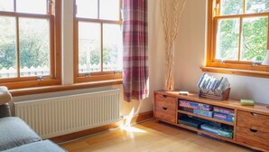Ein Zimmer mit großen Fenstern, einem Heizkörper, einer Holzkassette mit Gesellschaftsspielen und einem Vorhang.