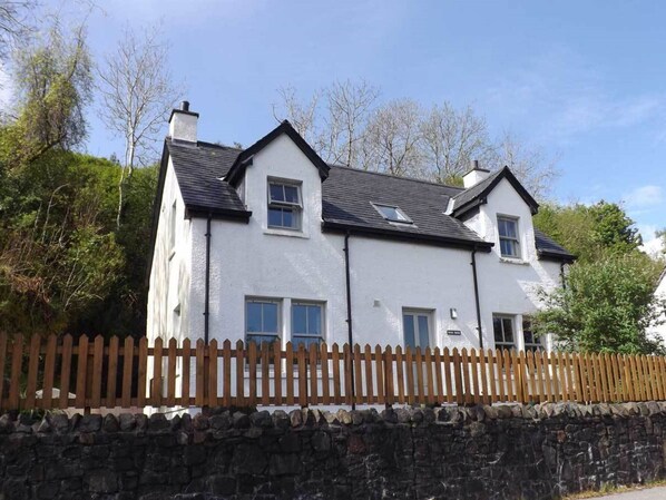 A two-story white building with a stone wall and wooden fence in front. - Staffin Road by Interhome (Mid Skye)