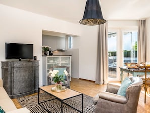 A modern living room with a flat-screen TV, a sofa, a coffee table, and a dining area with a table set for breakfast. - Junior Suite Modern by Interhome (Ascona)