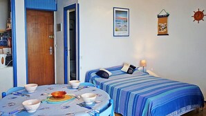 Una habitación con dos camas, una mesa de comedor con cuencos y cubiertos, y una pared con un cuadro enmarcado y un reloj.