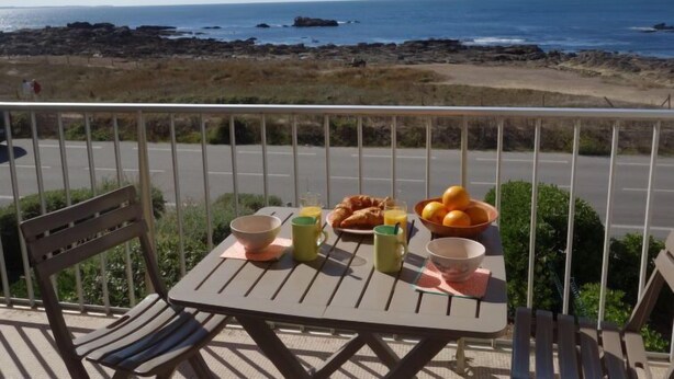 Mesa en balcón con alimentos para el desayuno y vista a la playa y el océano.