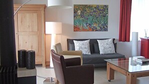 A modern living room with a sofa, armchair, and glass coffee table. There is a painting on the wall, a lamp, and a wooden cabinet. - Promenade Wohnung 21 by Interhome (Davos)