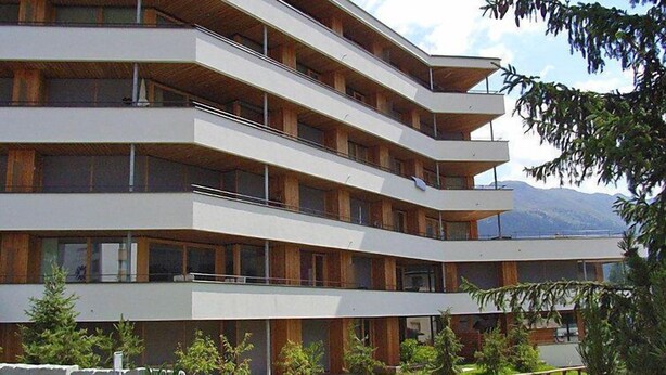 A multi-story hotel with balconies, a stone wall, and a view of mountains. - Promenade Wohnung 21 by Interhome (Davos)