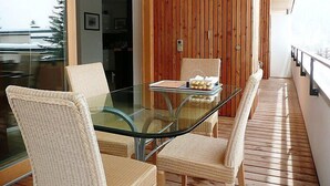 A modern balcony with glass-top dining table and wicker chairs, wooden flooring, and a wooden wall. - Promenade Wohnung 21 by Interhome (Davos)