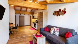 A modern living room with a grey sofa, wooden beams, a dining area, and a kitchen. - Mooslehen by Interhome (Kaprun)