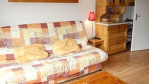 Une pièce chaleureuse avec un plancher en bois, un canapé à carreaux agrémenté de coussins, une armoire en bois et une lampe rouge.