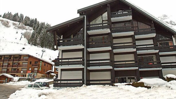 Un hôtel à plusieurs étages doté de balcons, avec une piste de ski en arrière-plan et un paysage enneigé.
