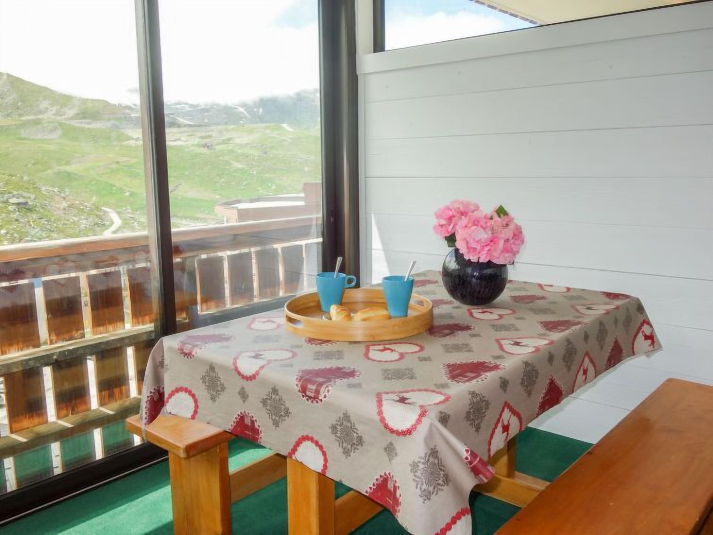 Un balcon avec une table dressée pour le petit-déjeuner, un vase rempli de fleurs roses et une vue panoramique sur des collines verdoyantes.
