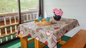 Een balkon met een ontbijttafel, een vaas met roze bloemen en een weids uitzicht over groene heuvels.