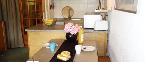 A compact kitchen with wooden cabinets, a sink, a toaster, and a vase with flowers on the counter.