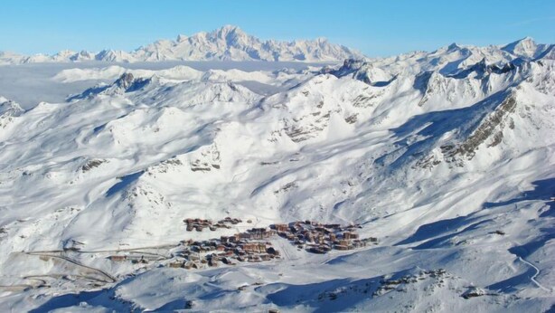Eine verschneite Berglandschaft mit einer kleinen Siedlung im Vordergrund.