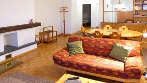 Una sala de estar con un sofá, una mesa de centro, una mesa de comedor con sillas, una estantería y una chimenea.