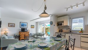 A modern kitchen with white cabinets, a microwave, and a sink. There is a dining table set with plates and glasses. - Le Parc des Druides by Interhome (Carnac)