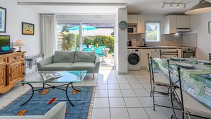 A compact living space with a sofa, a glass-top coffee table, a dining table with chairs, a washing machine, and a kitchen area. - Le Parc des Druides by Interhome (Carnac)