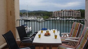 Een balkon met een tafel gedekt voor twee, met uitzicht op een jachthaven vol boten en een hotel op de achtergrond.