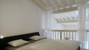 Een slaapkamer met een bed, witte gordijnen en uitzicht op de lucht.