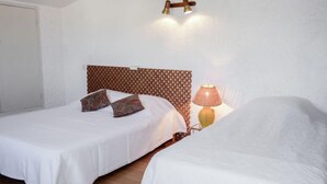Habitación de hotel con dos camas, cabecero de madera, lámpara de pared y una puerta.