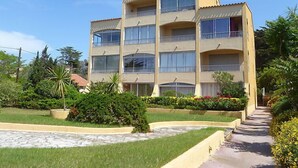 Un edificio de varios pisos con balcones, rodeado de jardines cuidados y un camino pavimentado.