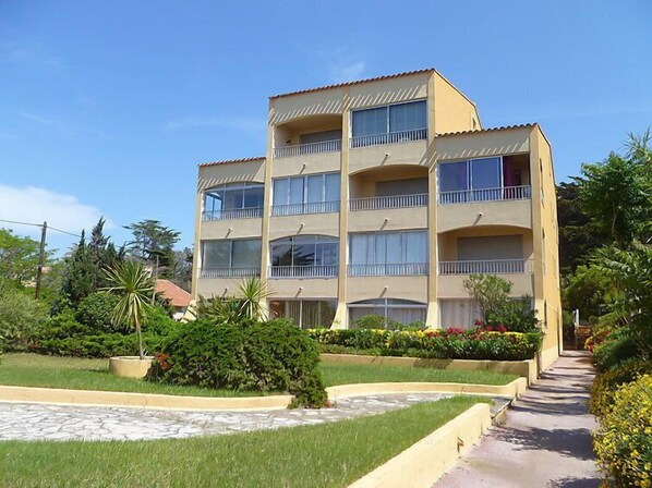 A multi-story building with balconies, surrounded by well-maintained gardens and a paved walkway.