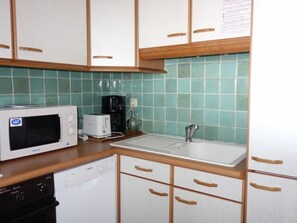 A compact kitchen with white cabinets, a microwave, a toaster, a coffee maker, and a sink.