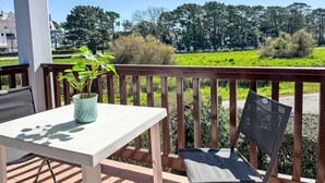 A balcony with a table and chair, a potted plant, and a view of a green field and trees. - Plein Ciel by Interhome (Carnac)