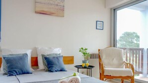 A hotel room with a bed, pillows, a rolled towel, a small table with a plant and glasses, a chair, and a large window with a view. - Plein Ciel by Interhome (Carnac)