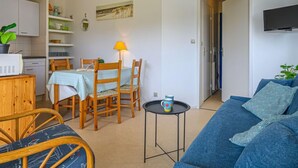 A cozy living room with a blue sofa, wooden chairs, a small round table with a mug, and a kitchen area with cabinets and a microwave. - Plein Ciel by Interhome (Carnac)