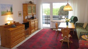 A room with a wooden cabinet, a dining table with chairs, a sofa, and a large window with a view of greenery. - Fellhornstrasse by Interhome (Oberstdorf)