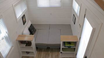 A compact room with a bed, two small wooden shelves, and a window with blinds.